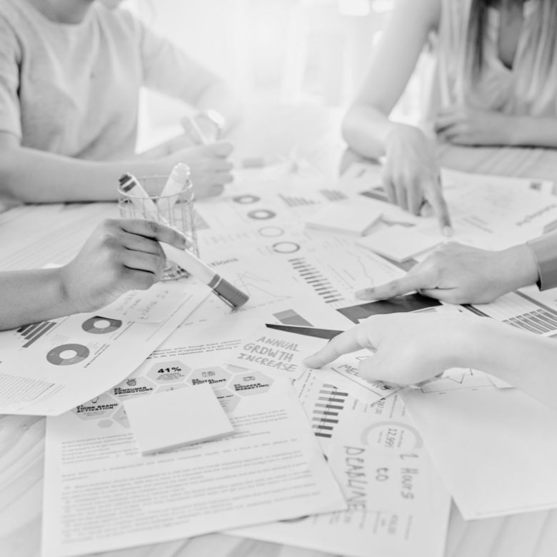 Business professionals analyzing charts, graphs, and data reports spread across a table in black and white