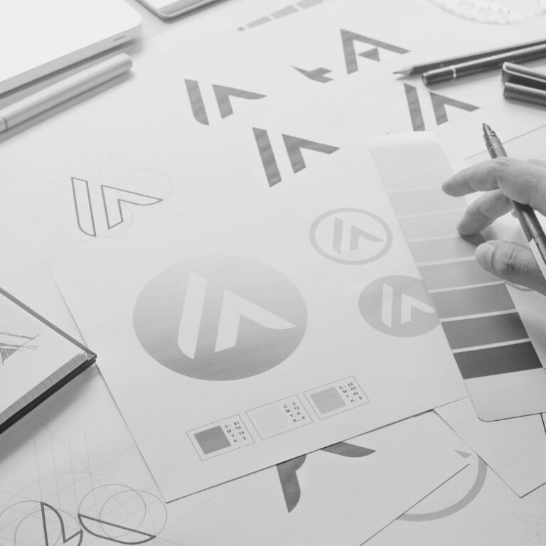 Hand sketching logo designs on paper with various brand identity concepts and design elements visible