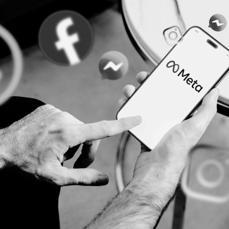 Hands holding smartphone displaying Meta logo with Facebook icons visible in blurred background